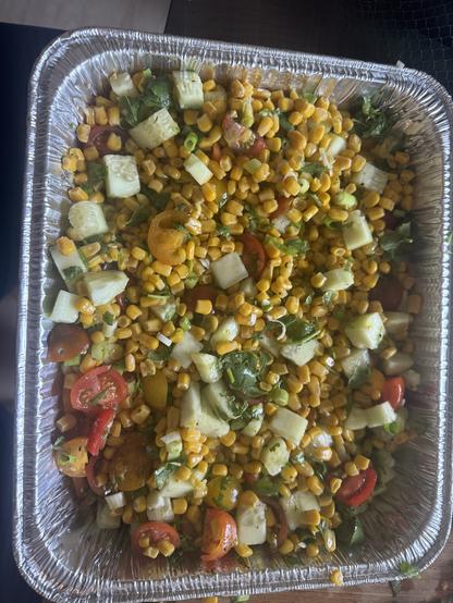 A delicious tray of yellow corn, red tomatoes and green cucumber mixed up .