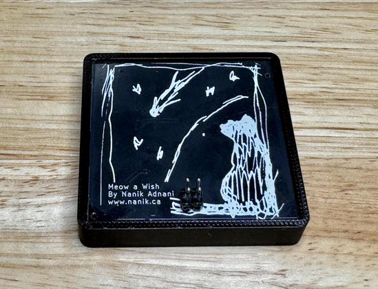 Black PCB with an abstracted sketch of the cat and night sky in white silkscreen. Text on the bottom left reads: 
Meow a Wish
By Nanik Adnani
www.nanik.ca