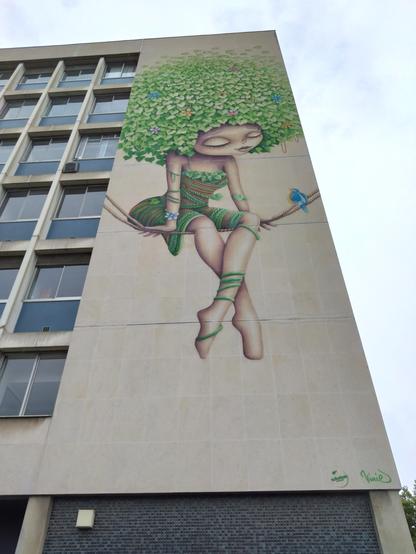 A 6 story high mural depicting a woman siting on 2 ropes talking to a small blue bird, with voluminous hair made out of plants.