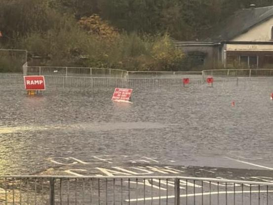 Floodwater covers Cwmbwrla roundabout in Swansea, with road closed signs standing in deep water.