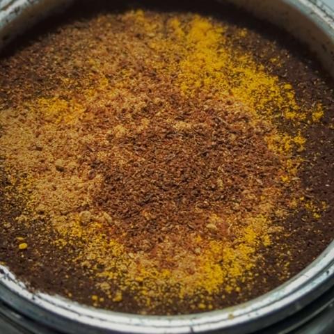 A close-up of Coffee grounds with orange turmeric, pumpkin pie spice, and ground cloves on top. They are packed in a moka pot filter set in the base, the threads visible around the side.