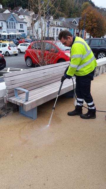 Council worker using specialist cleaning equipment on Mumbles Prom to remove stains beneath new benches.