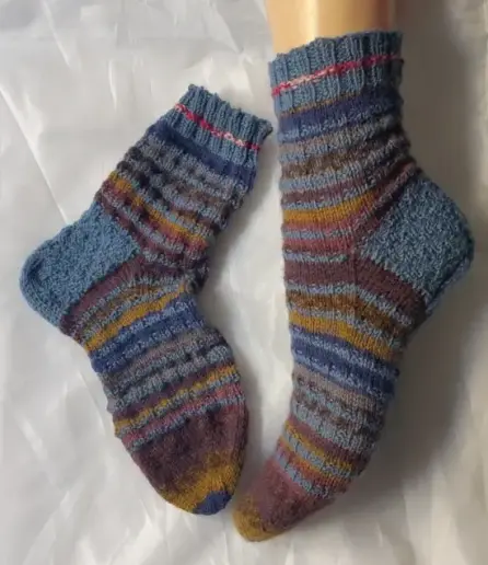 Paire de chaussettes tricotée avec des rayures bleues et dans des tons bruns, bleu et ocre. L'une est à plat, l'autre, à droite, sur une jambe de mannequin de vitrine pour montrer la différence entre les deux aspects.