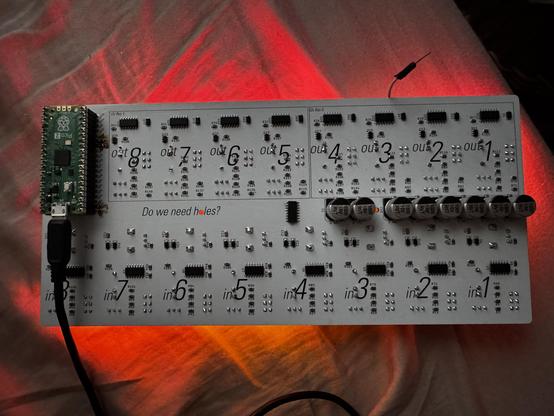 The back of a white circuitboard, with labels on each section. In channels 1-8. Out channels 1-8. They're divided into sections 12C bus 0 and 12C bus 1.
On the left is a Raspberry Pi Pico2 that communicates between the board and the host computer. On the right are a line of large capacitors to supply servos with power and keep them from corrupting data with their current draw.