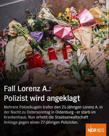 Blumen, Kerzen und Grußbotschaften liegen an einer Gedenkstelle, viele bunte Sträuße, Teelichter und Karten. Es wirkt wie ein Ort des Trauerns und Gedenkens.

Text im Bild:
„Fall Lorenz A.: Polizist wird angeklagt. Mehrere Polizeikugeln trafen den 21-Jährigen Lorenz A. in der Nacht zu Ostersonntag in Oldenburg – er starb im Krankenhaus. Nun erhebt die Staatsanwaltschaft Anklage gegen einen 27-jährigen Polizisten.“