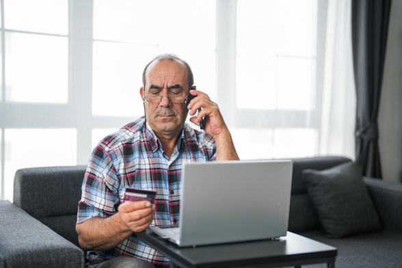 Un hombre estafado hablando por teléfono con una tarjeta de crédito en la mano. (Getty Images)