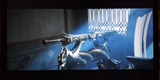 The Dormant Dragon Sword in its sheet, resting on its stand. The stand is shaped like two Chinese dragons twirling around each other, with their wings supporting the sword, and iy looks like it's cast in bronze.