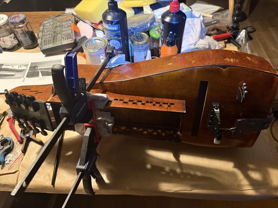 Photo of the hurdy gurdy on its side witg glue clamps holding down the key box.