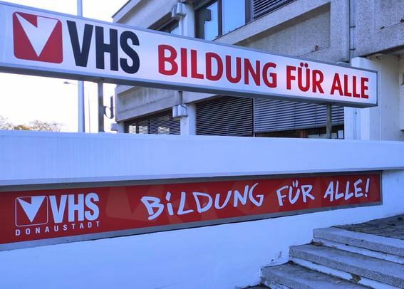 Stiegenaufgang. Seitlich angebracht zwei Schilder mit der Aufschrift VHS. Bildung für alle.