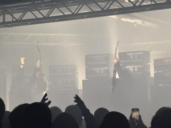 A band with to guitarist raising their axes in sync, a lot of amplifiers in the background