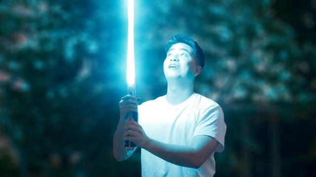 A person holds an illuminated retractable lightsaber with a blue blade.
