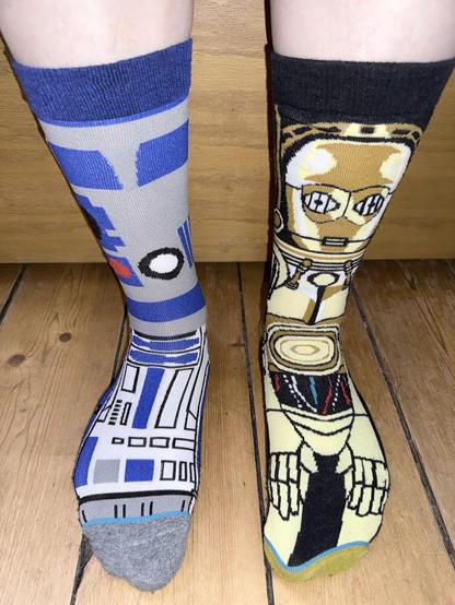 A man’s legs from shins down. He has an R2-D2 sock on his right foot and a C3PO sock on the left.
