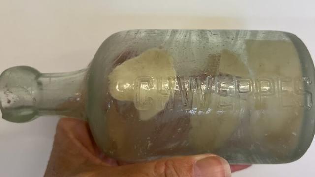 An old bottle with "CHWEPPES" embossed on it and some pieces of paper inside the bottle.