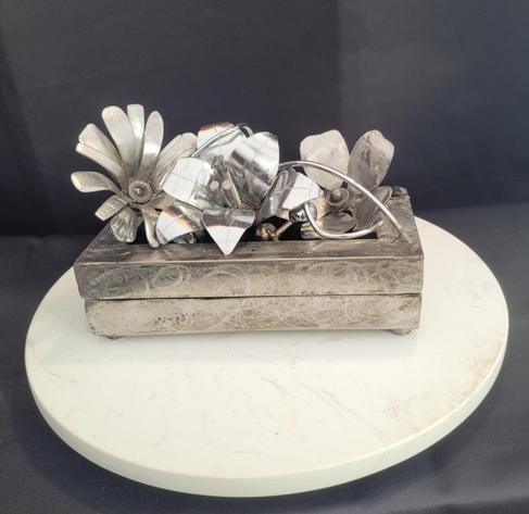 Coffret fleuri 

Un coffret en acier recyclé. Il mesure environ 25cm x 10cm. Il y a 3 fleurs sur le dessus. Il est poli donc brillant.