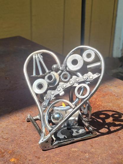 Un chandelier en forme de coeur en acier recyclé. On voit des washers, des clous, une partie de scie à chaîne, des boulons, bearing, etc...

Son ombre ainsi que sa projection font magie !