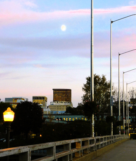 Scène de la vie urbaine : un pont et des lampadaires, des édifices à l’arrière-plan, la pénombre qui s’installe, un ciel magnifique aux teintes pastel.
© 2025, Chartrand Saint-Louis, photographie
