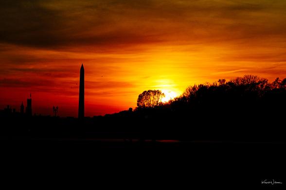 Washington Monument obelisk stands against dramatic sunset over National Mall trees