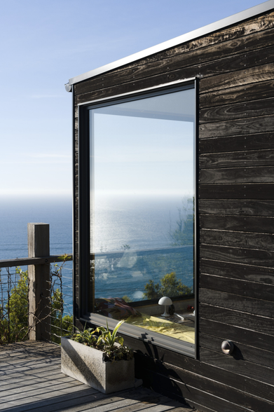 A blackened wooden outdoor wall looking through two windows to the ocean behind.