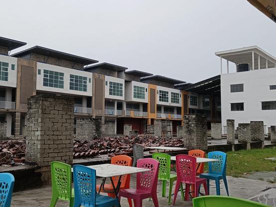 Colourful plastic chairs and tables of a restaurant contrasting with the grey ruins of a paused construction site.