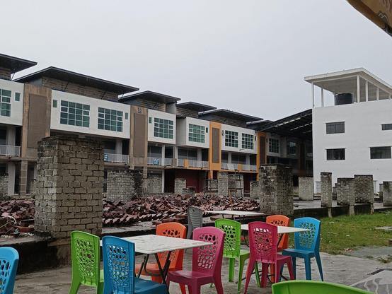 Colourful plastic chairs and tables of a restaurant contrasting with the grey ruins of a paused construction site.
