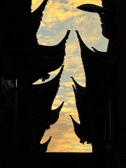 Silhouettes of traditional Chinese rooftops rise sharply against a golden sunset sky, their curved eaves framing the warm clouds glowing with evening light.