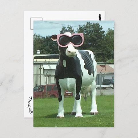 product image of a postcard with a photo of a giant fiberglass Holstein cow wearing overlarge pink sunglasses on the side of the road.