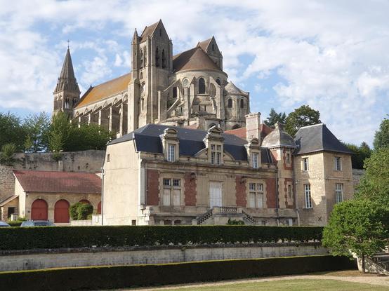 Vue sur l'église de Saint-Leu-d’Esserent en hauteur, et une grande maison traditionnelle au premier plan en dessous.