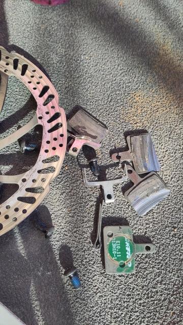 Plaquettes et disque de frein de vélo sur un plancher gris
Les plaquettes sont usées bien au delà du raisonnable et ont endommagé le disque