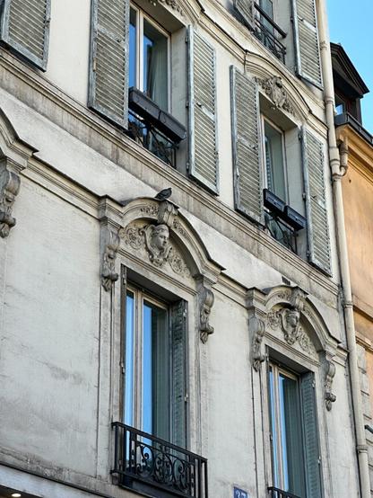 tall French-style windows with shallow wrought iron balconies and carved ornamentation on the side of a stone building.