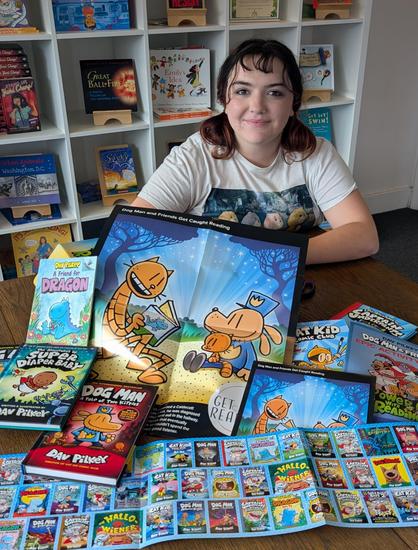 Intern Olivia posing with multiple posters and titles by author Dav Pulley.