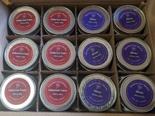 Top-down view of a cardboard box with inner cardboard dividers separating round jars of wine jelly made from Cab Franc and Shiraz. Note: I did not buy all this jelly, just four jars....