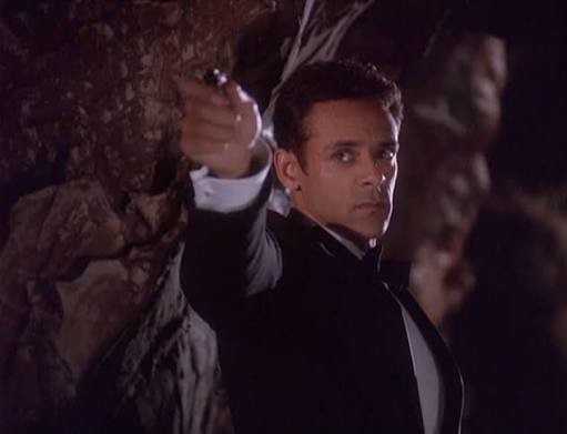 Bashir wearing a tux in a cave and pointing a pen gun