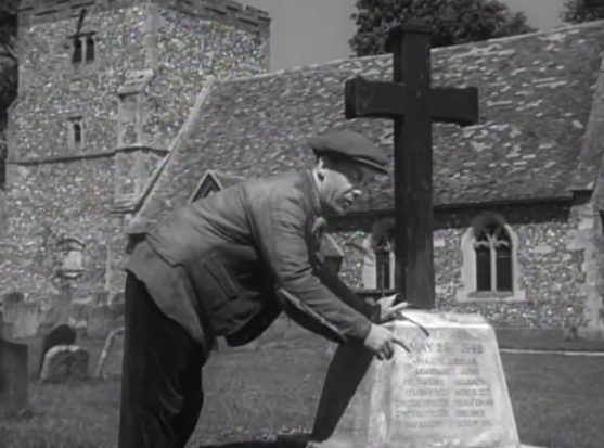 A scene from the promo for the movie "Went The Day Well", a tale of plucky English ordinary folk repelling an insidious invasion by forces of Nazi Germany. A middle-aged man with a pipe and flat cap bends over a memorial stone in a graveyard pointing at the name son the memorial. He is wearing a flat cap, this seems significant somehow