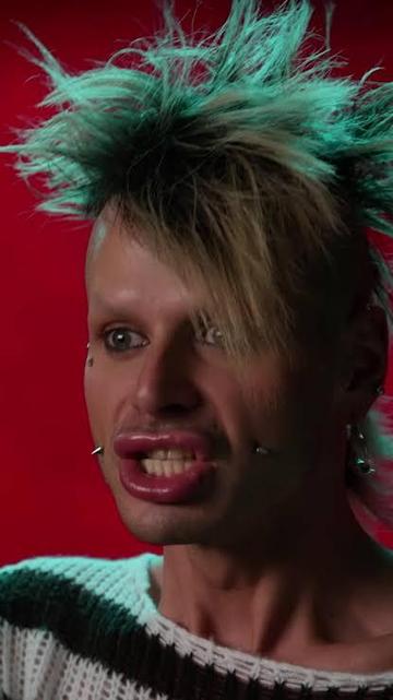 A white man with short, spikey blond hair, metal studs in the cheeks