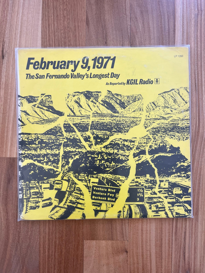 A vinyl album cover in yellow with black images and words that read “ February 9, 1971. The San Fernando Valley‘s longest day. As reported by KGIL radio.” The image of the valley and freeway is interrupted by large jagged rifts to convey the San Fernando earthquake damage.