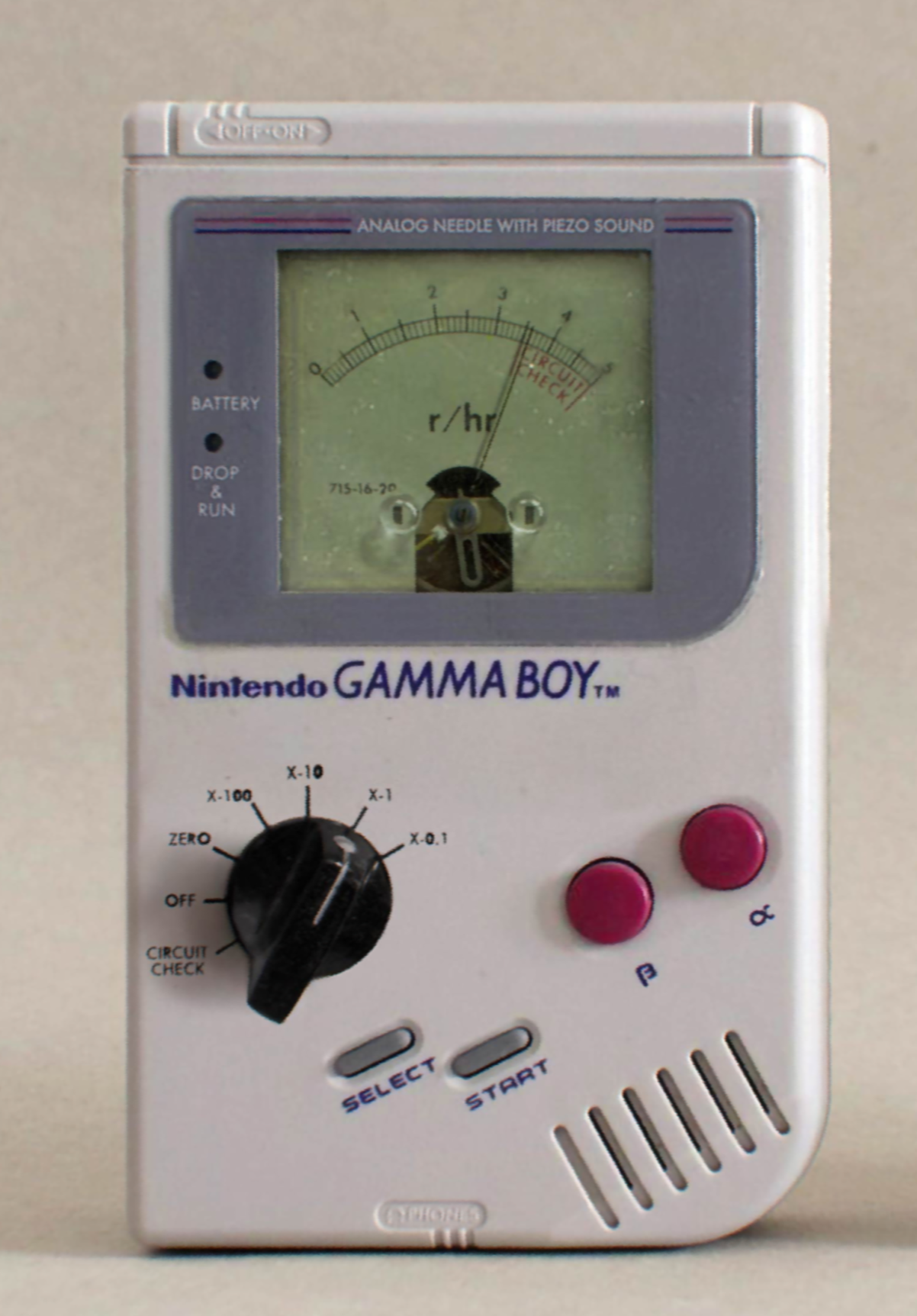 A picture of a Nintendo Gamma Boy. It's kind of a geiger counter but looks just like a nintendo Game Boy. It has a Select, Start, and a knob to select options, and a Beta and Alpha button in that reddish pink. On screen is a little needle showing up to about 3.6 roentgen. to the left of the screen is a Battery and a Drop & Run indicator.