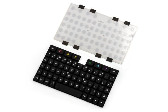 A photo of the KeebDeck Keyboard keypad and dome sheet. The dome sheet has many domes visible through the white plastic, and 8 black pieces of tape to cover where the backlight LEDs would be. The Keyboard has 69 keys with the usual PC layout, and a few extra ones color symbols and colors.