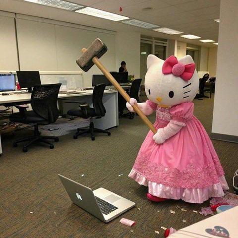 Meme photo. In a drab soulless office setting with depressing fluorescent lighting and depressing brown industrial carpet, a person in a Hello Kitty costume - an enormous white cat head with a pink bow on one ear and a pink sparkly dress - wields a sledgehammer at an open laptop on the floor at their feet.