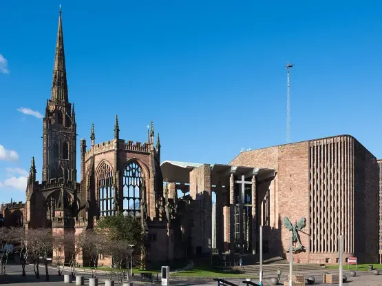 The image shows a prominent architectural scene featuring two distinct buildings. On the left, there is a tall, spired structure that appears to be a historical church or cathedral, known for its intricate design and gothic elements. On the right, there is a modern building with a more contemporary architectural style, characterized by smooth lines and a large open space.

The background is clear with a blue sky, and there are trees and other elements in the foreground, contributing to the overall setting. This location represents a blend

Image Credits: Wikimedia / DeFacto / CC BY-SA 4.0
