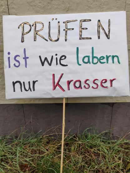 Ein Demoschild ist an einer Hauswand gelehnt, darauf steht "Prüfen ist wie labern nur krasser"