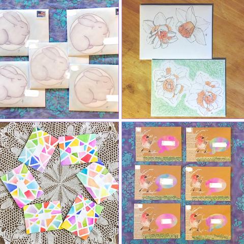 A collage of four photos of various types of mail art: hazy pastel drawings of sleeping bunnies inside a circle, detailed pen and watercolor wash drawings of fancy daffodils, multi colored watercolor shapes like stained glass with bare white lines separating/defining their shapes, Collage of a hand drawn and painted bird in a tree covered in words over grass made of sheet music splattered green, singing a multicolored watercolor speech bubble for the address, all on brown paper.