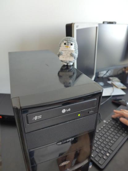 Une peluche d'un pingouin positif sur une tour de PC avec des écrans en arrière plan