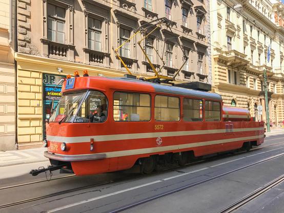Eine ältere rote Straßenbahn bei der in der hinteren Hälfte das Dach fehlt und stattdessen ein Tank oder ähnliches verbaut ist.