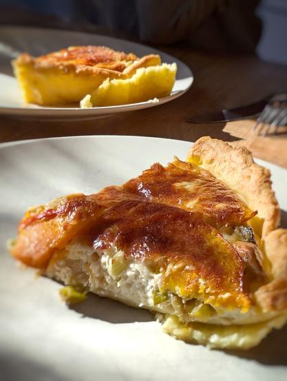 in Stück Kürbis-Lauch-Tarte mit goldbrauner Oberfläche auf einem hellen Teller, im warmen Sonnenlicht. Foto by Johann Seidl, Freisinger Gartenblog.