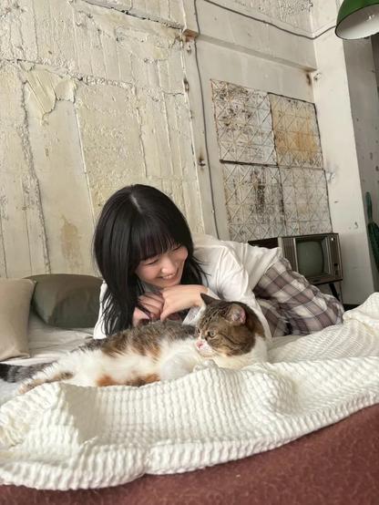 A woman smiling laying on a bed looking at a cat.