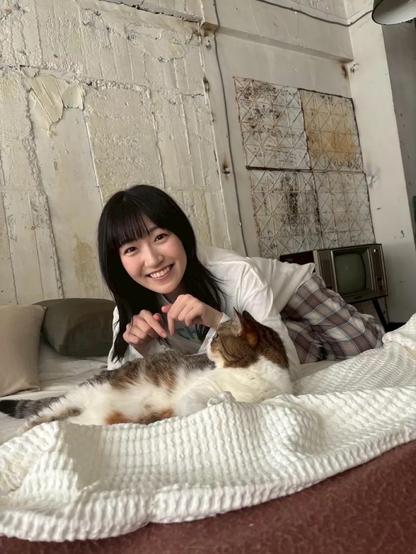 A woman smiling laying on a bed looking at a cat.