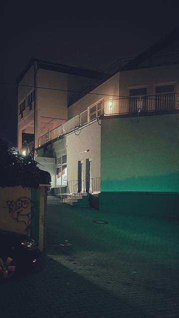 Early night in a suburban setting. Green light, concrete road, a building right in the frame. A parked car left.