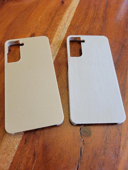 Two 3D printed phone cases. The one on the left looks very plasticky. The one on the right almost looks like sanded wood, only with no grain.