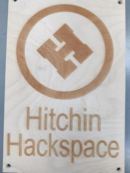 At the top of the image is the Hitchin Hackspace "H" logo in the centre of a circle. The H is at 45 degrees and the character has a square outline. The words "Hitchin Hackspace", along with the H in the circle, are laser engraved on to an A4 sized sheet of Birch plywood.
It should be at the pub, to help identify us, providing one of our members remembers to bring it!🤦‍♂️