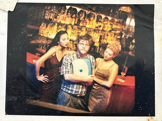 Old MacAddict photo of two hot women and a young magazine nerd holding a blue iBook to his chest.